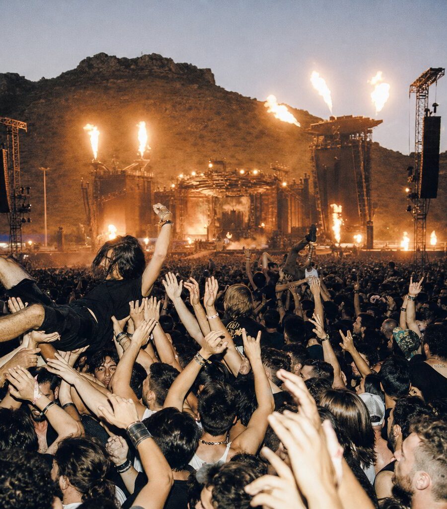 Multitud con las manos en alto ante el escenario principal de un festival de rock en España al atardecer