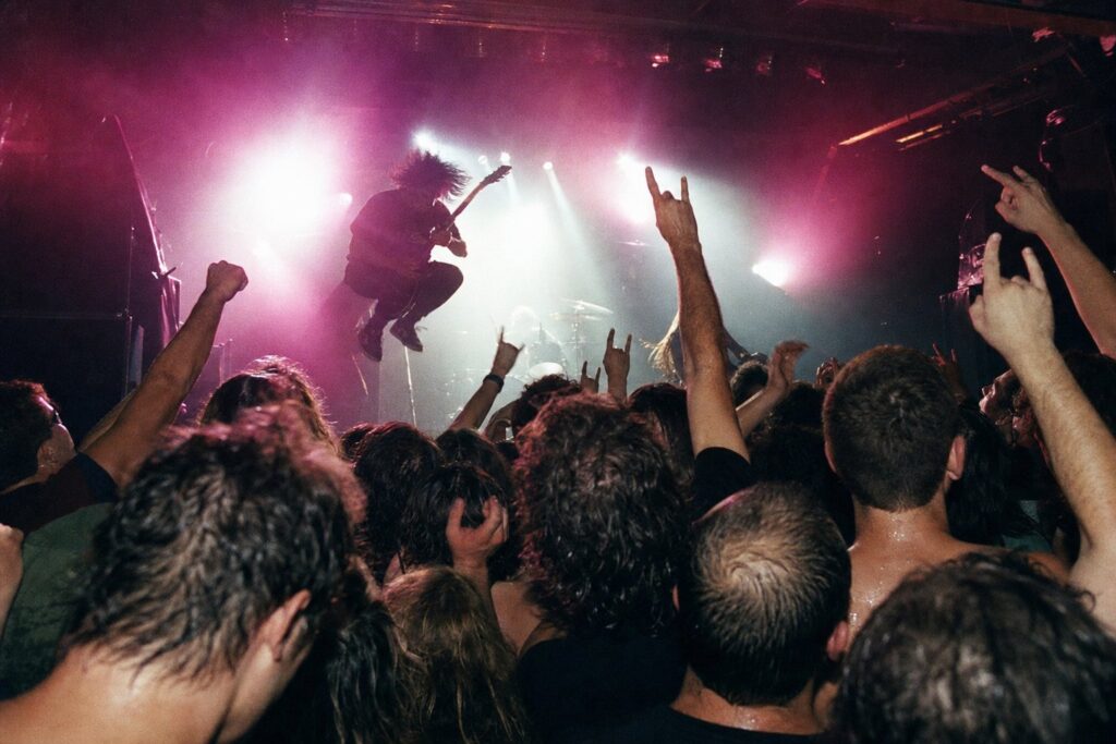 Público en primera fila de un concierto de rock en una sala pequeña, entre luces de escenario