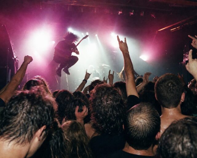 Público en primera fila de un concierto de rock en una sala pequeña, entre luces de escenario